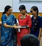 Volunteer woman handing a device or paper to two visually impaired girls, showing support in education.